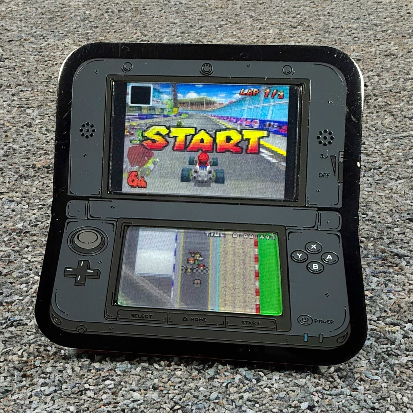 Black handheld gaming console displaying a racing game on two screens.