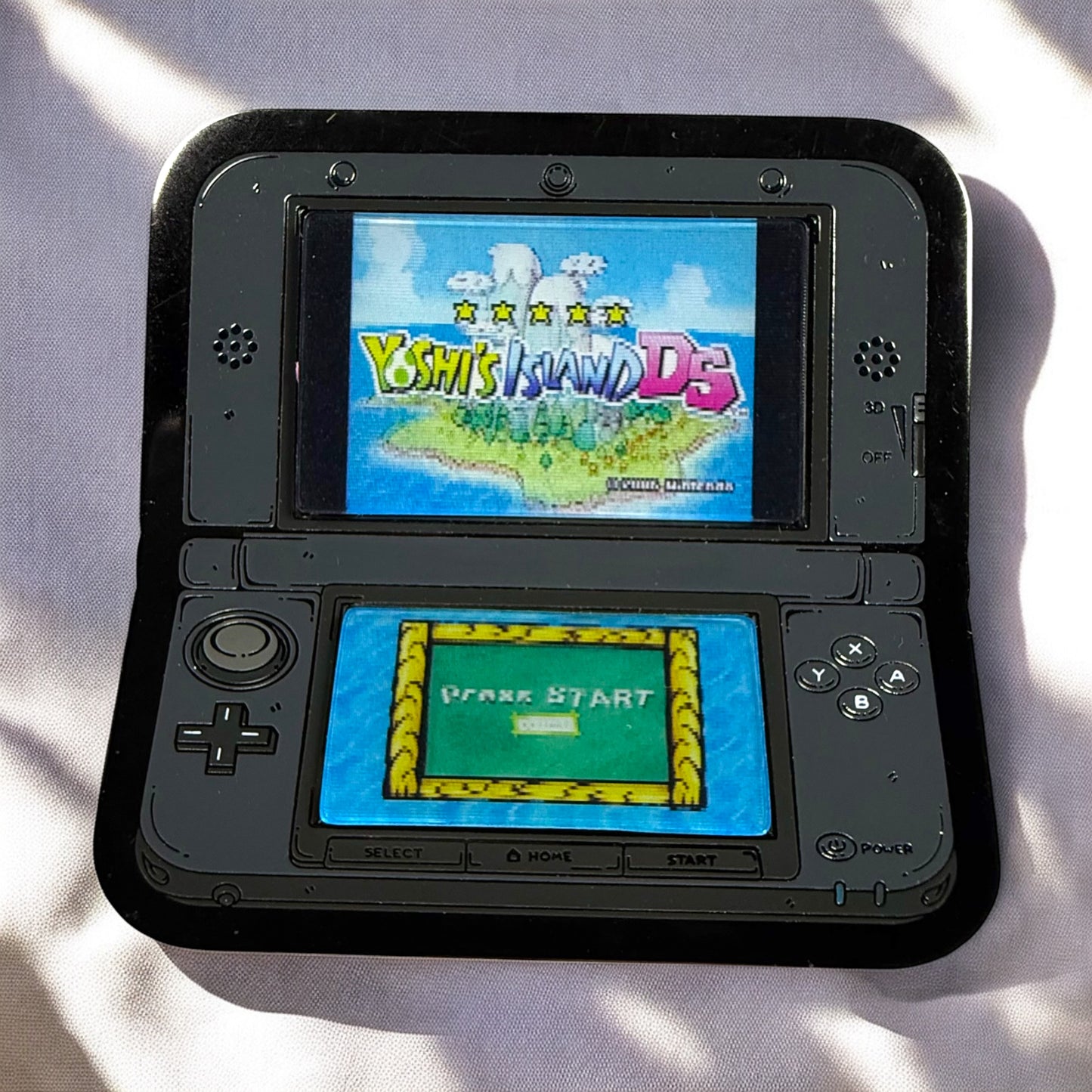 Black handheld gaming console displaying 'Yoshi's Island DS' on a light background