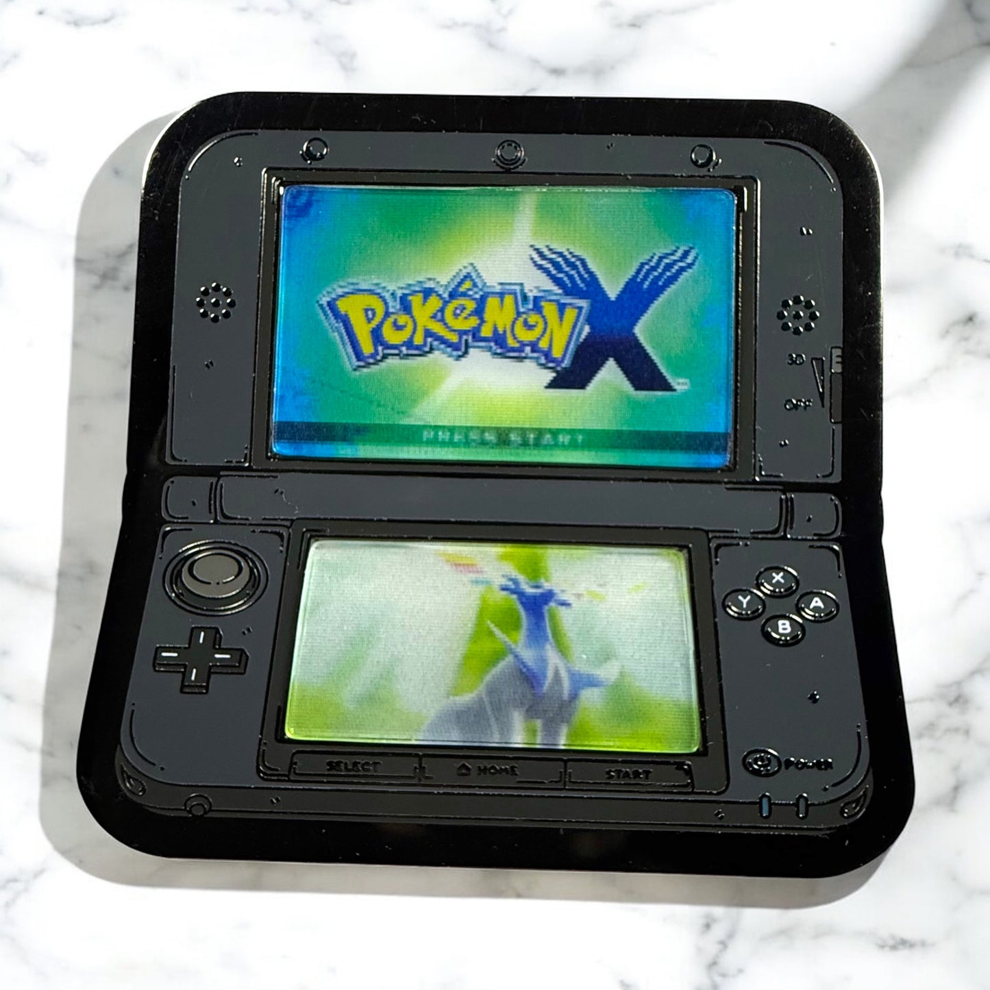 Black handheld gaming console displaying 'Pokémon X' on a marble surface