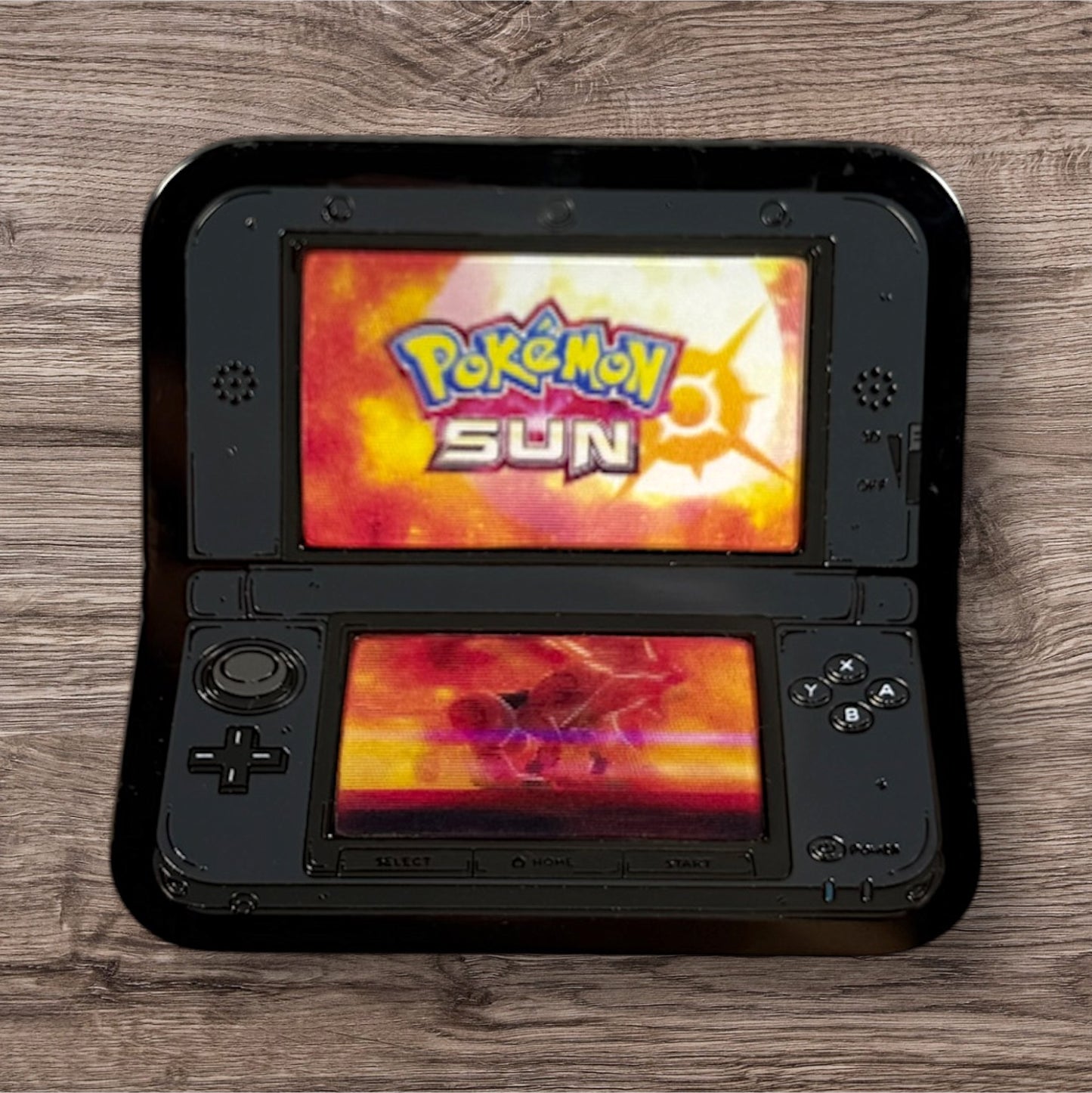 Black handheld gaming device displaying 'Pokémon Sun' on a wooden surface
