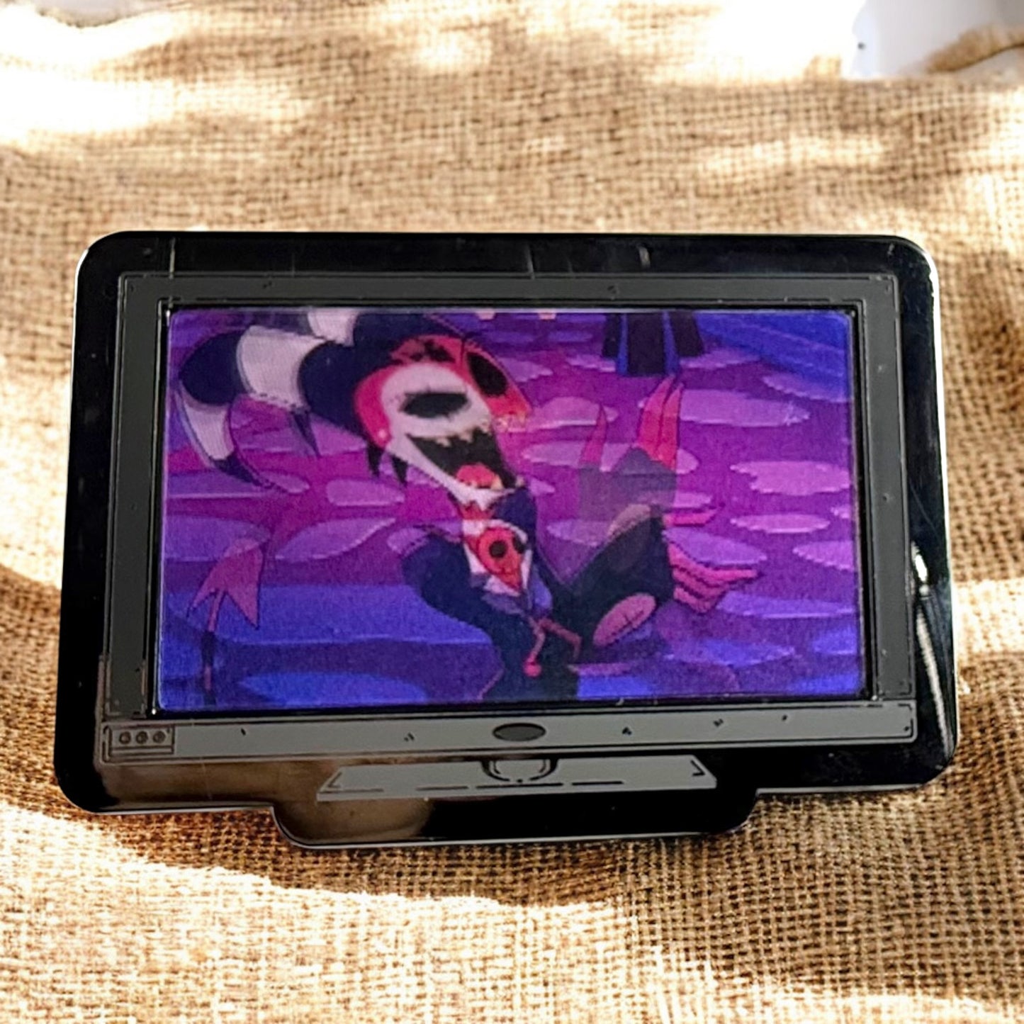 Small screen displaying a colorful character on a textured fabric background