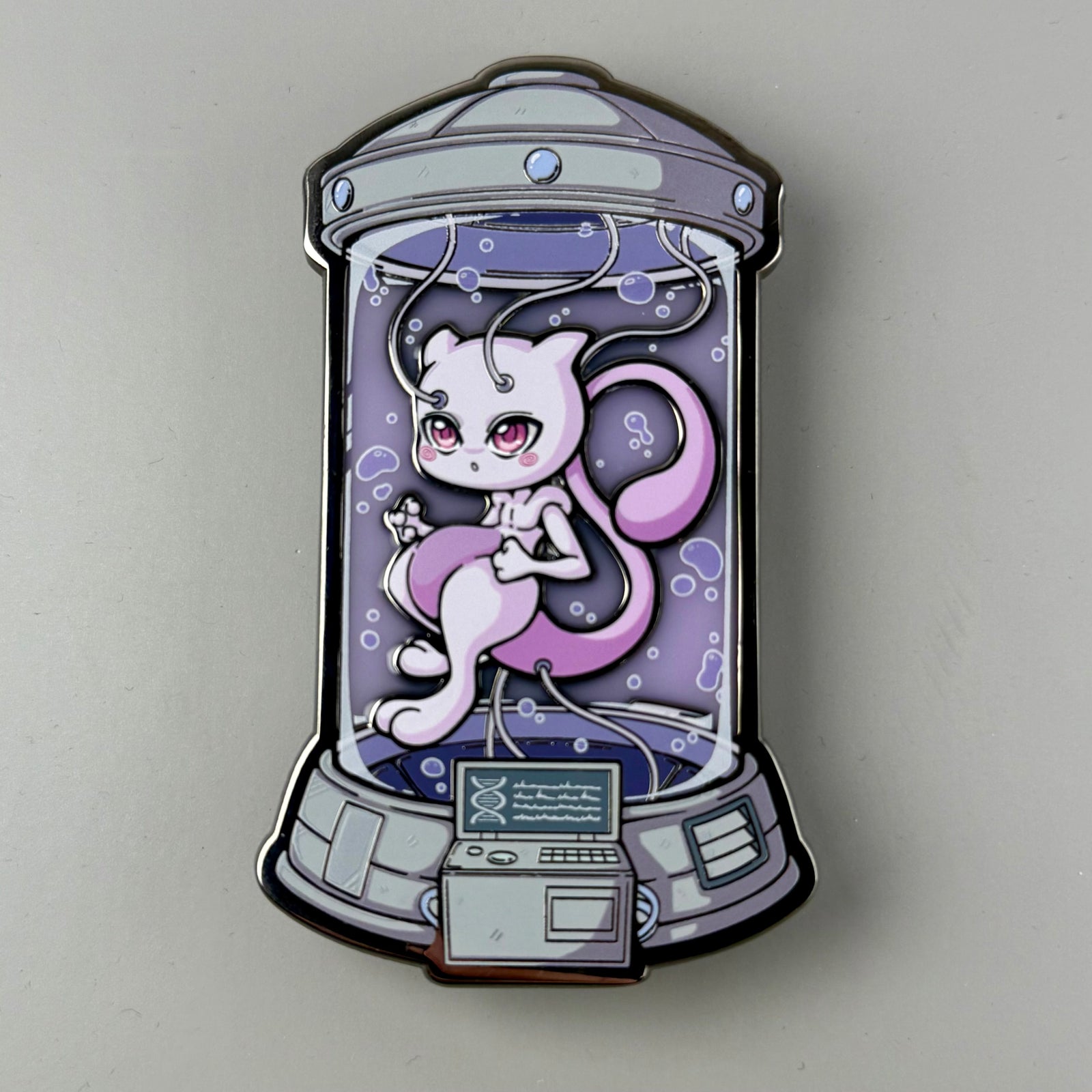 Enamel pin with a Mewtwo character in a glass jar on a gray background