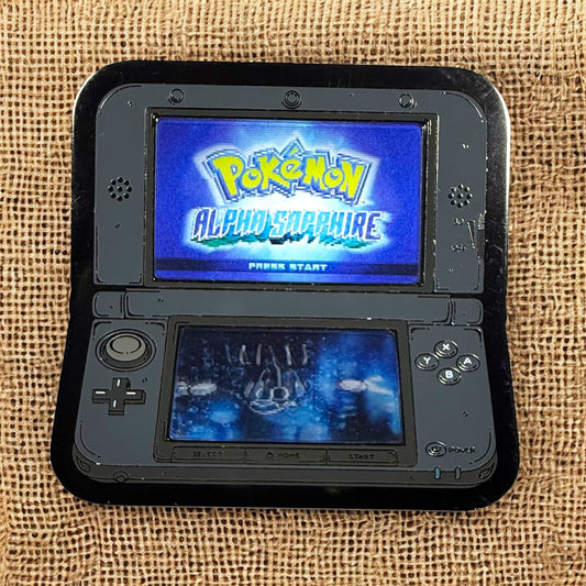 Nintendo 3DS gaming console displaying 'Pokémon Alpha Sapphire' on a textured fabric background