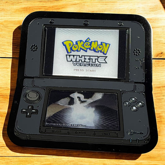 Black handheld gaming console displaying 'Pokémon White Version' on a wooden surface