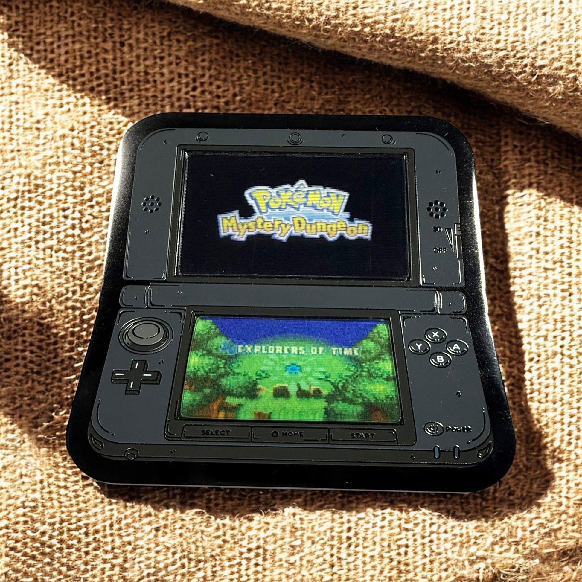 Handheld gaming console displaying 'Pokémon Mystery Dungeon' on a textured surface