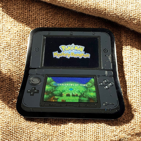 Handheld gaming console displaying 'Pokémon Mystery Dungeon' on a textured surface