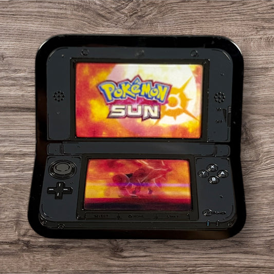 Black handheld gaming device displaying 'Pokémon Sun' on a wooden surface