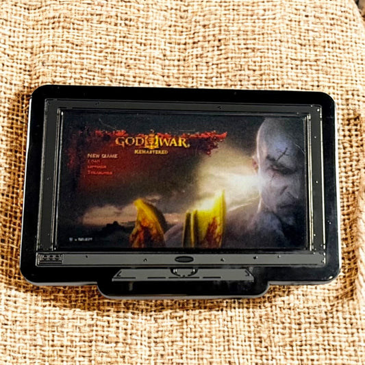 Portable screen displaying 'God of War' game cover on a textured surface