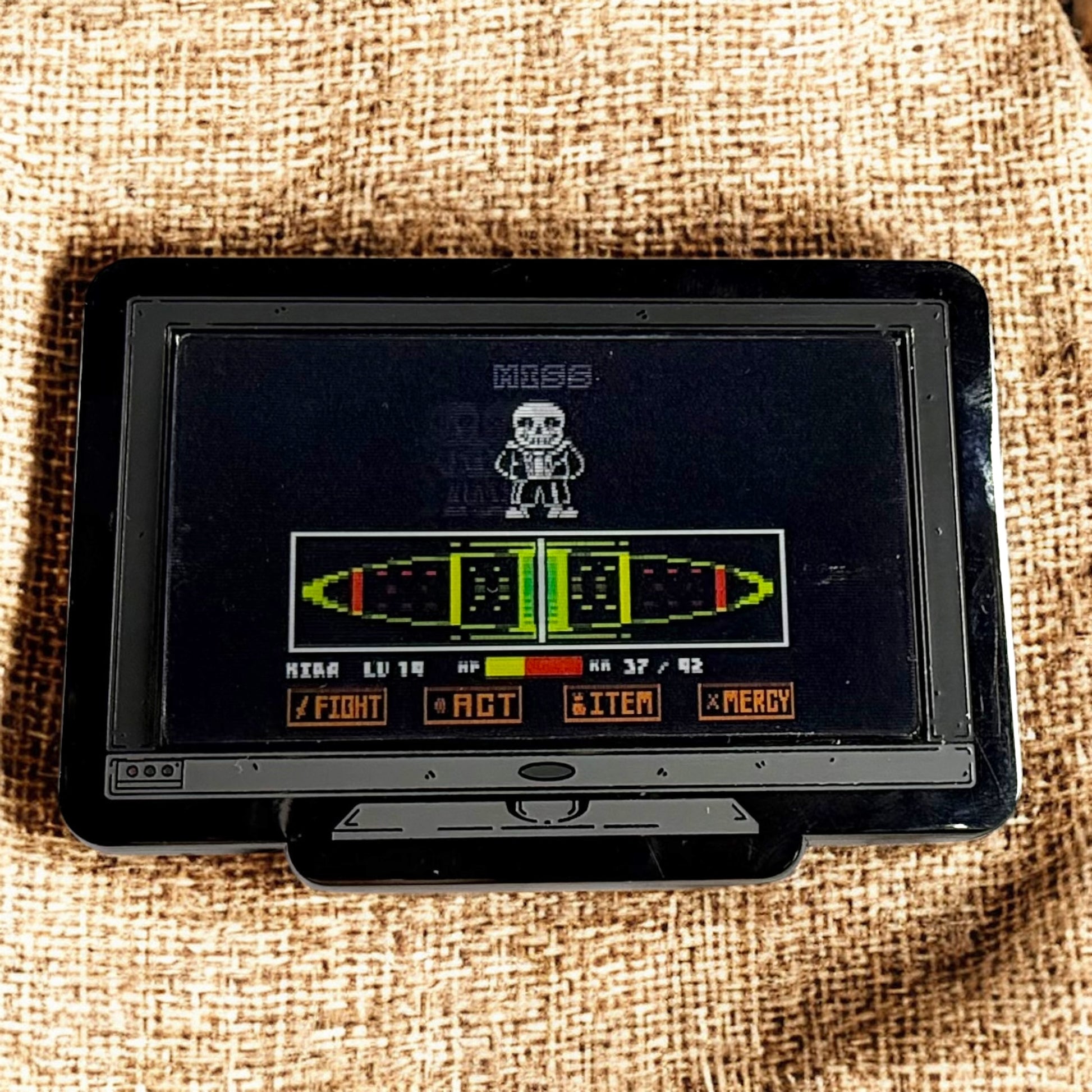 Vintage handheld gaming console with a screen displaying a game interface on a textured fabric background.